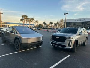 A Tesla Cybertruck and a Cadillac Escalade, often seen in Orlando limousine service fleets, are parked side by side in a parking lot outside a Tesla dealership.